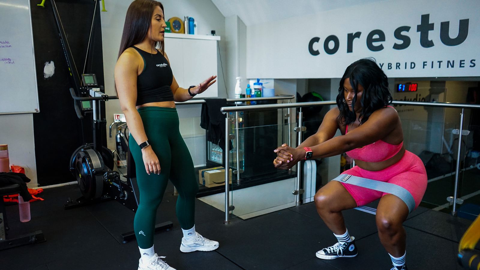 A Core Studio coach guiding a member through banded squats on the studio floor in Blackheath SE3